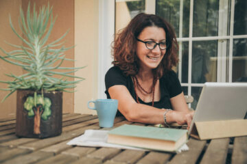 Femme souriante utilisant une tablette électronique sur une table en bois dans la cour extérieure d'une maison