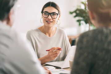 Femme souriante tenant un crayon et discutant avec deux personnes au bureau