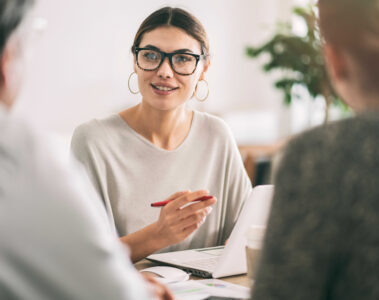 Femme souriante tenant un crayon et discutant avec deux personnes au bureau