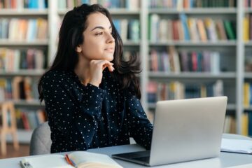 Étudiante assis derrière son portable qui prend une pause et qui réfléchit